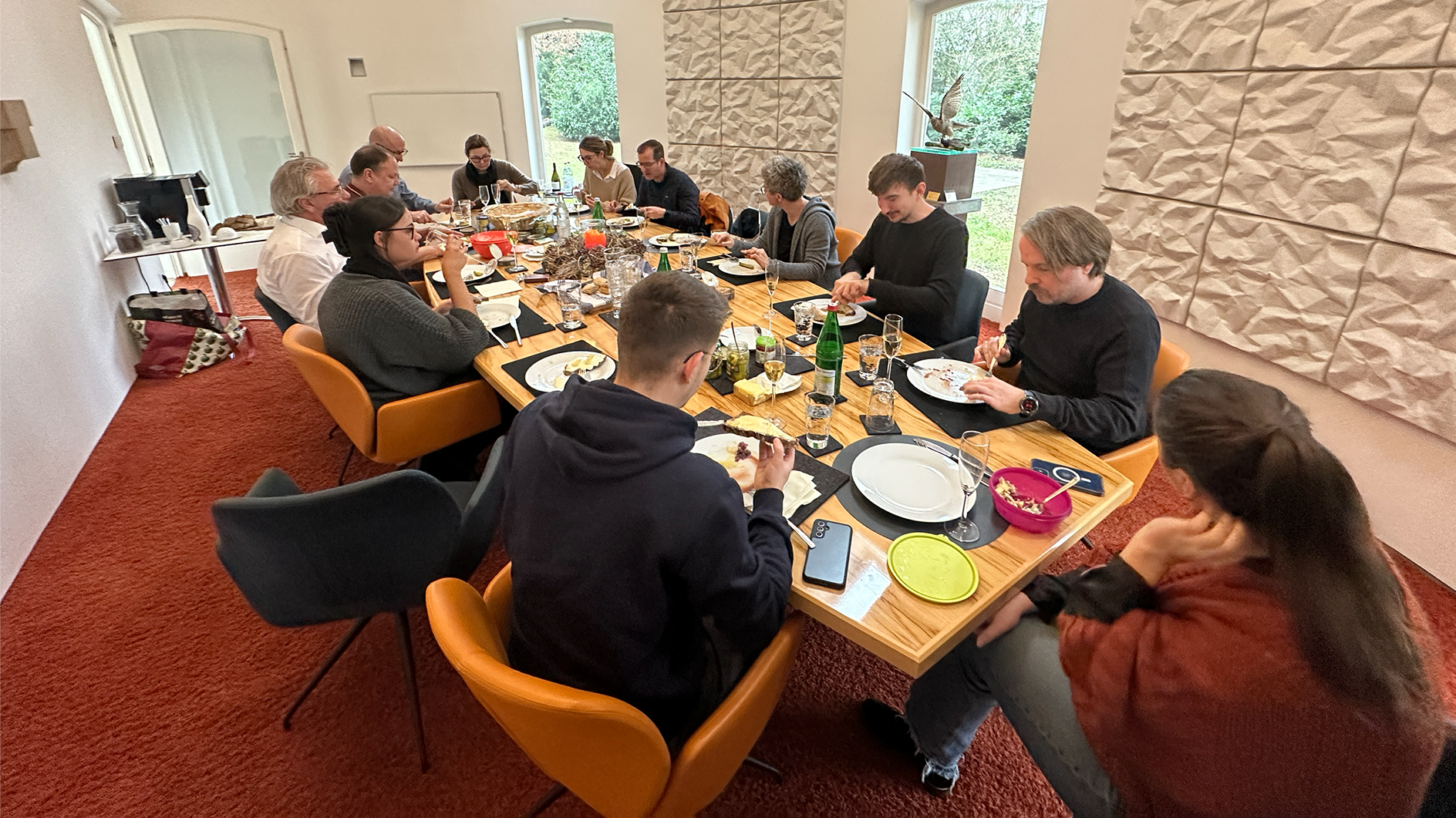 Gemeinsames Mittagessen im Meetingraum Das Bild zeigt etwa 10 Personen beim Mittagessen an einem Konferenztisch in einem Besprechungsraum. Die Atmosphäre ist sehr offen und angenehme.